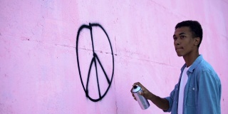 惊恐的少年用喷漆在墙上画和平符号，阻止种族主义