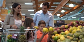 快乐的拉丁美洲家庭在超市购买杂货，孩子们选择水果加入购物车