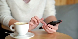 女人在餐桌上写作，喝咖啡或茶。她一边搅拌杯子一边看手机。特写镜头