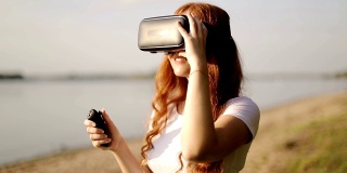 带着VR眼镜和耳机的红发小女孩正在用遥控器观看360度视频。
