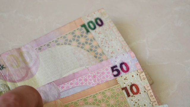 一只手伸出来，伸向呈扇形分布的卡塔尔现钞，这种货币被称为卡塔尔里亚尔(Qatar Riyal)现钞，在白色的背景上散开。金钱交换。
