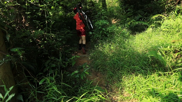 女自行车手背着山地车在热带森林小径的斜坡上行走