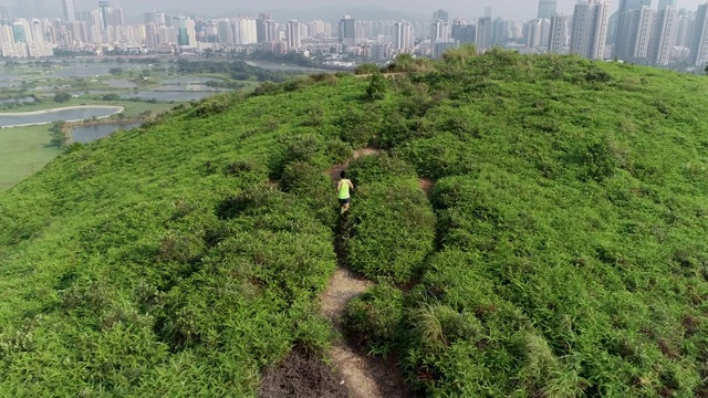 女超级马拉松运动员在现代城市旁边的山上奔跑的鸟瞰图