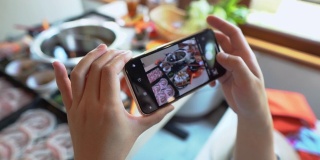 白天，在一家餐馆里，一位女士的手正在用智能手机拍摄日本火锅