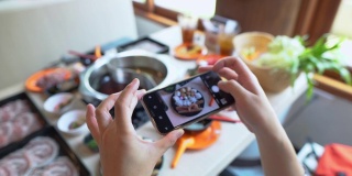 白天，在一家餐馆里，一位女士的手正在用智能手机拍摄日本火锅