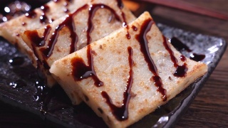 在餐厅将黑酱油倒在即食的美味萝卜糕上，这是中国传统的地方菜萝卜糕。视频素材模板下载