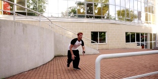 一个肌肉发达的年轻人正在表演跳过楼梯栏杆的特技。特技人，跑酷，自由奔跑的概念。以现代建筑为背景