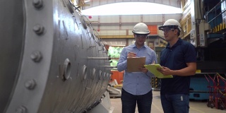 冶金工厂的工程师在检查建筑结构，并在剪贴板上做笔记