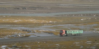 一辆旧卡车在空旷的公路上飞驰，穿过风景秀丽的西藏平原。