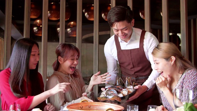 快乐的服务员带着火锅和海鲜在餐厅招待一群朋友。