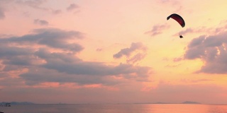 盖伊在蔚蓝的天空和美妙的海滩上飞行着滑翔伞红色的风筝，极限活动港口。感觉像鸟儿一样自由。概念克服了人类生理的限制。