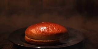 木桌子上放着一个黑色玻璃盘子里的汉堡面包，背景是水蒸气。资料片。特写镜头