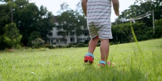 亚洲小女孩训练走路，坐在绿色的草地上玩耍，母亲节的概念，慢镜头。