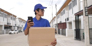 拿着包裹盒子的快递员在村屋用智能手机寻找顾客
