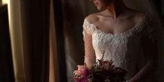 新娘手持花束，在婚礼前透过窗户看