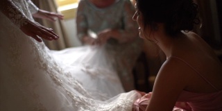 伴娘(妈妈和姐姐)帮助新娘为婚礼穿衣服