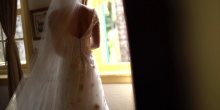 新娘手持花束，在婚礼前透过窗户看