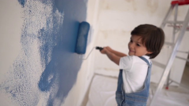 可爱的小男孩喜欢在家里用油漆滚筒画画，面带微笑