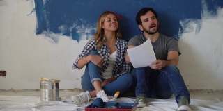 一对幸福的夫妇坐在地板上看着纸上的设计在家庭装修期间