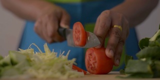近距离拍摄的女人的手切西红柿在木砧板上的健康食物在桌子上。