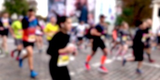 在慈善城市马拉松赛期间，许多人在城市街道上跑步的模糊剪影的特写。参赛者运动员在城市的街道上跑很长的距离。慢动作。