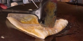 烤饼制作，通过烤饼机将面粉和油脱粒。印度传统街头小吃。泰国煎饼、香蕉和鸡蛋。泰国街头小吃和甜点。制作烤肉点心