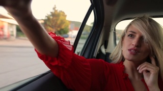 年轻的金发女子一边开车一边用智能手机自拍视频素材模板下载