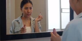 美丽的亚洲女人在镜子前用口红化妆，快乐的中国女性使用美容化妆品提高自己准备在家里的浴室工作。生活方式女性在家放松的概念