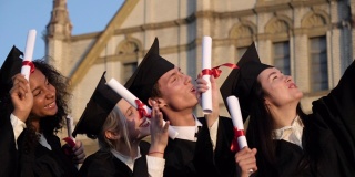 毕业的混血儿们穿着黑色传统长袍，戴着帽子，在智能手机上自拍