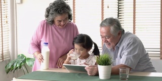 亚洲小女孩喝牛奶和玩平板电脑上的数字一起在家里的烹饪室。技术、家庭和教育的概念。4 k决议。