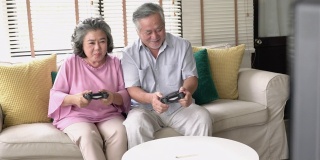亚洲成熟的老年人在家里的客厅玩电子游戏快乐和激动的情绪。用操纵杆控制游戏。家庭、科技、娱乐、放松的理念。