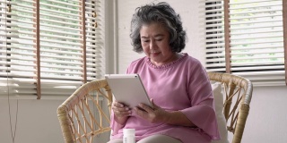 亚洲成熟的资深女性在家中从平板电脑上搜索信息医学。科技、医疗、健康、制药的生活理念。4 k决议。