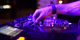 DJ手控制音响控制台，用于迪斯科俱乐部的混音。手指触摸按钮滑块，甲板上播放电子音乐。夜总会舞会上的彩灯。用慢动作拉近镜头