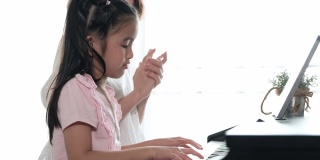 亚洲母亲和她的女儿一起弹钢琴的慢镜头。母亲带着幸福和微笑，拍着手教女儿。