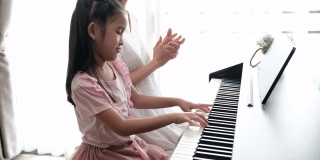 亚洲母亲和她的女儿一起弹钢琴的慢镜头。母亲带着幸福和微笑，拍着手教女儿。