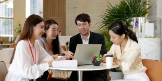 一群商务人士在现代设计办公室里开会，他们用笔记本电脑和纸质文件交谈