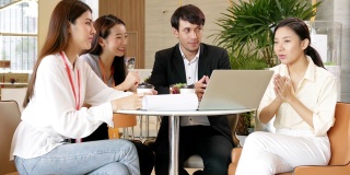 一群商务人士在现代设计办公室里开会，他们用笔记本电脑和纸质文件交谈