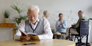 架上集中了三位老人，两位老年妇女和坐轮椅的残疾老人，在养老院打牌。戴眼镜的聪明老人在餐桌上看书思考