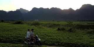 女孩和男孩骑摩托车在日落的田野鸟瞰