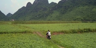 夫妇骑摩托车沿着崎岖的道路在田野鸟瞰