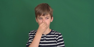 一个小男孩用手指捏着他的鼻子在绿色的屏幕上