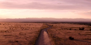 新墨西哥沙漠公路的乡村景象:夕阳下，汽车行驶在一条土路上
