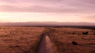 新墨西哥沙漠公路的乡村景象:夕阳下，汽车行驶在一条土路上视频素材模板下载