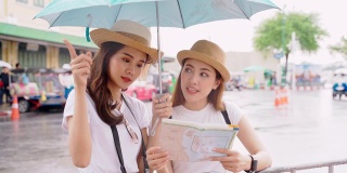 女人和朋友在看地图。亚洲女人享受曼谷Wat Pho的地标在曼谷市。在雨天，两名亚洲妇女撑着雨伞在泰国的主要寺庙中探险
