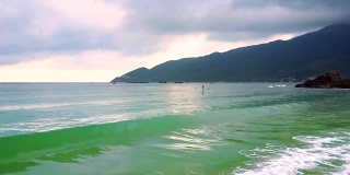 女孩在桨板上沿着海岸航行，泡沫的波浪在海滩上翻滚