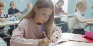 在小学课堂上，白种女孩在练习笔记中写作，参加考试和写作考试。初中教室与多样化的孩子努力工作和学习新东西