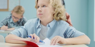 小学课堂:一个聪明可爱的白人男孩在练习笔记本上写字的肖像。初中教室与多元的聪明的孩子们努力工作，学习新东西