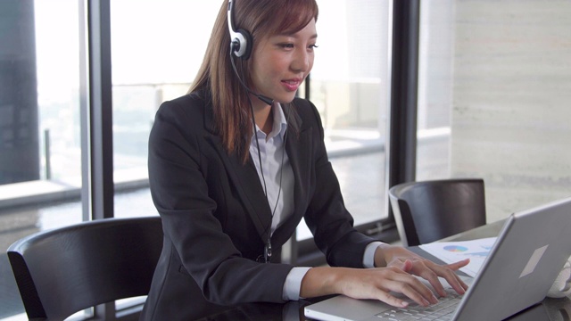 商务女性坐在办公室用耳机使用笔记本电脑工作
