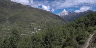 无人机飞向四姑娘山(四姑娘山)，山谷中有一个藏族小村庄(四姑娘山镇)。拍摄于前往海子谷的徒步路线上。
