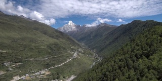 无人机缓缓地飞向四姑娘山(四姑娘山)，山谷中有一个藏族小村庄(四姑娘山镇)。拍摄于前往海子沟的徒步路线上。